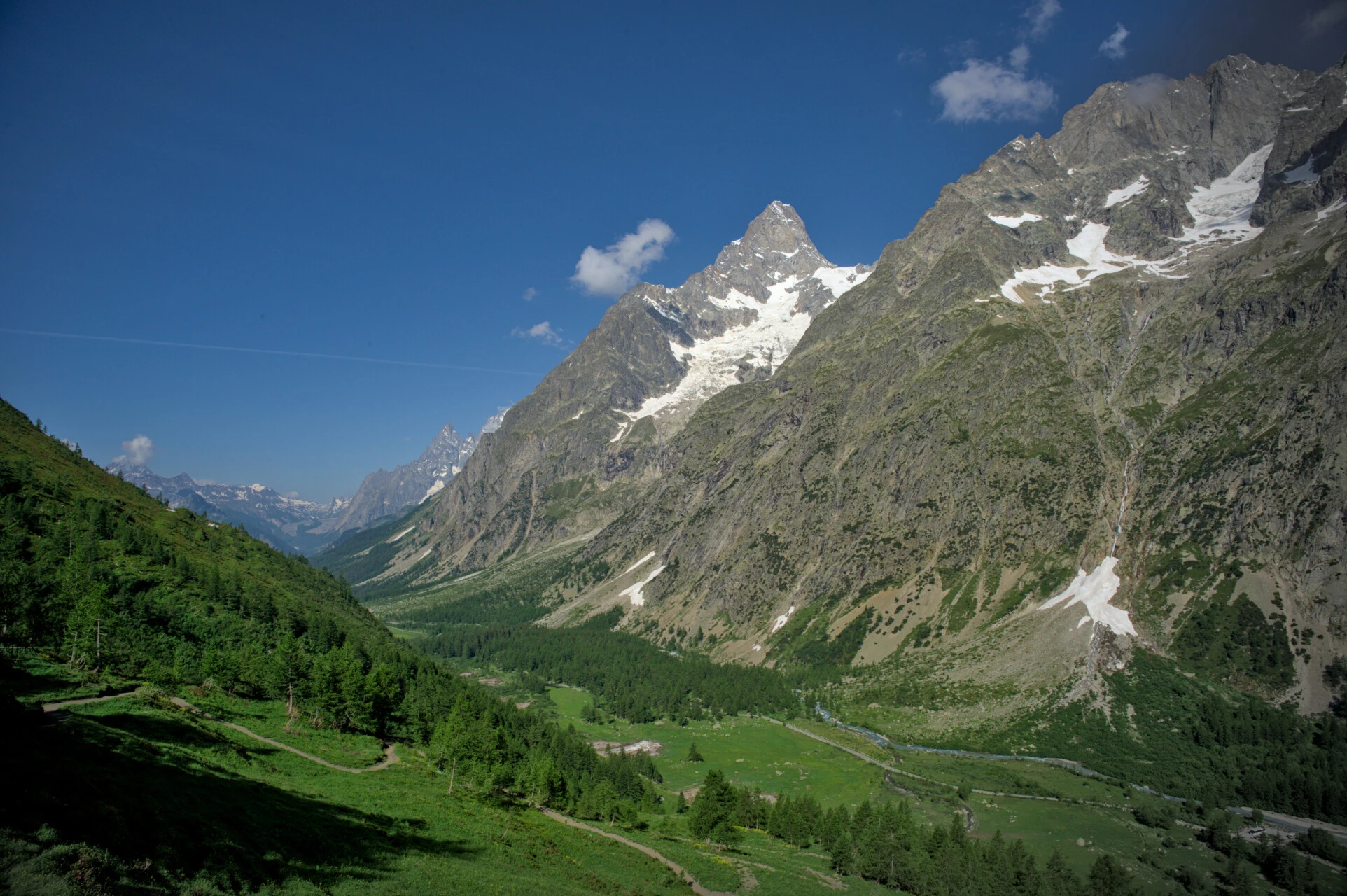 Dawn in the Italian Val Ferret, green meadows framed by larch trees and snowy summits
